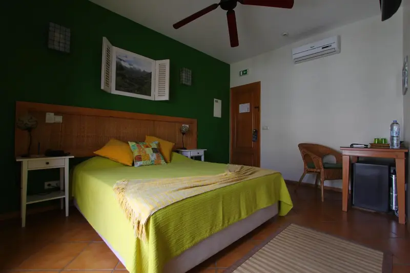Une chambre lumineuse avec un lit recouvert d'un plaid vert et de coussins colorés.