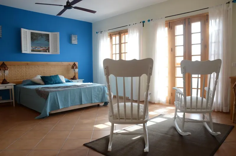 Une chambre lumineuse avec un grand lit et deux fauteuils en bois.