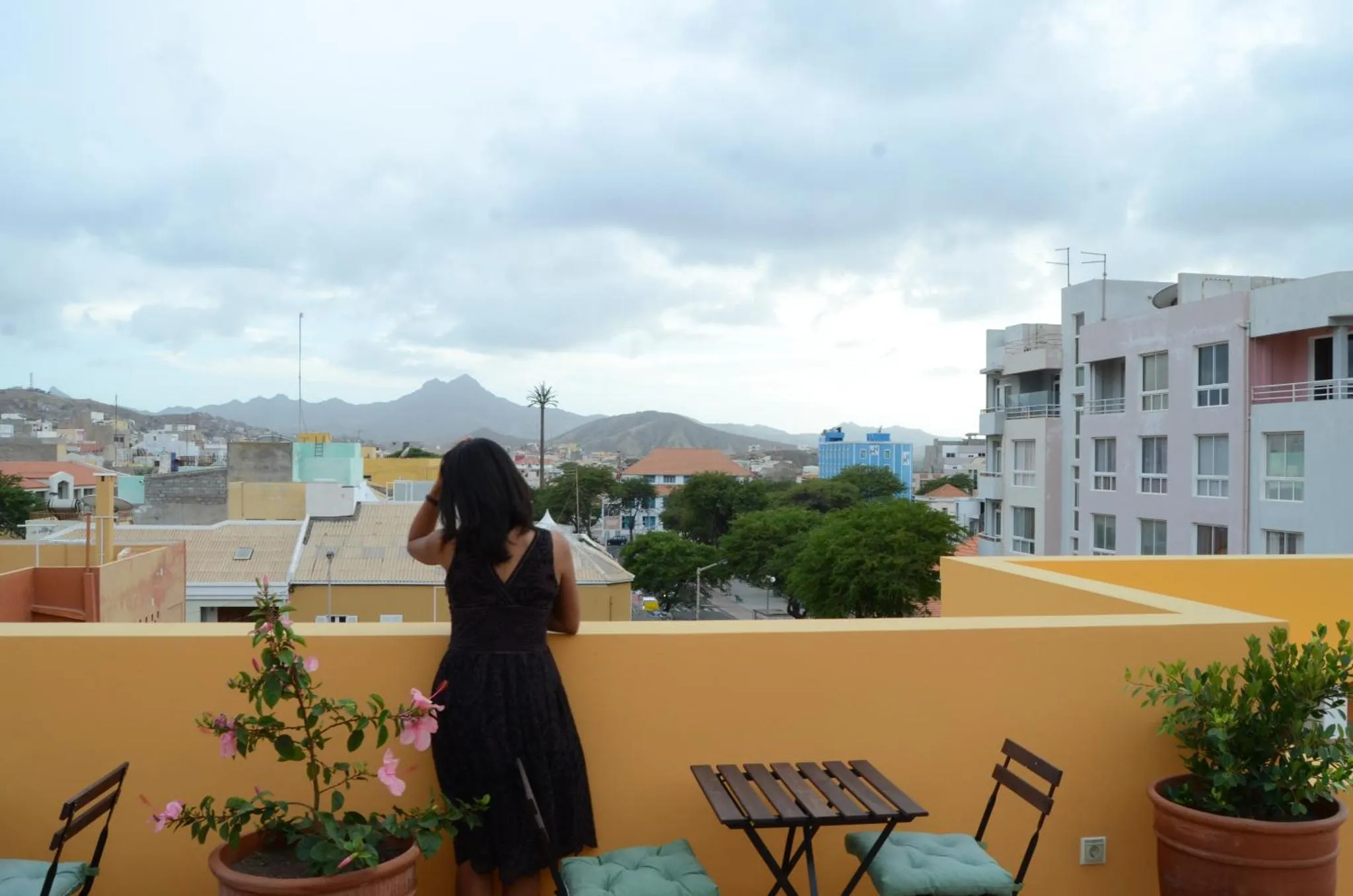 Une personne observe un paysage urbain et montagneux depuis une terrasse.