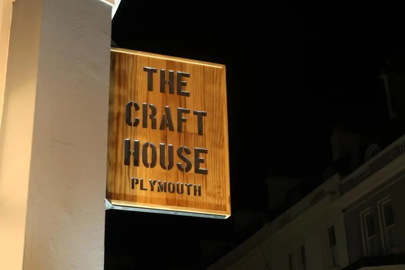 Enseigne lumineuse en bois indiquant un établissement nommé The Craft House à Plymouth.