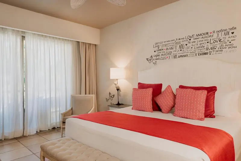 Une chambre lumineuse avec un grand lit recouvert d'une courtepointe rouge et de coussins.
