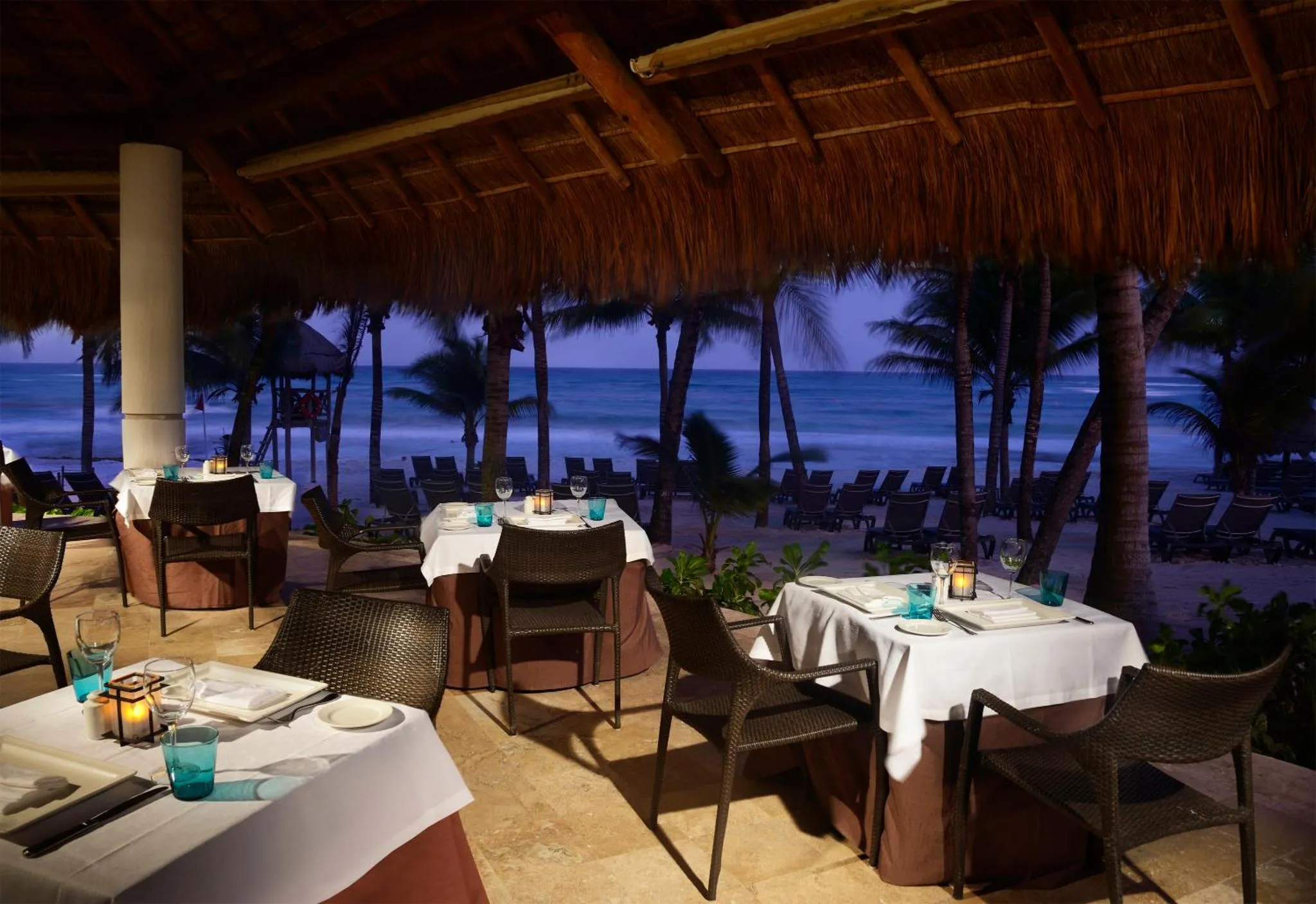 Tables dressées sur une terrasse en bord de mer au crépuscule.