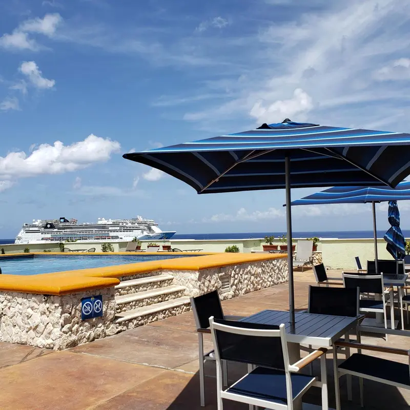 Terrasse avec parasols et vue sur la mer et un navire de croisière.