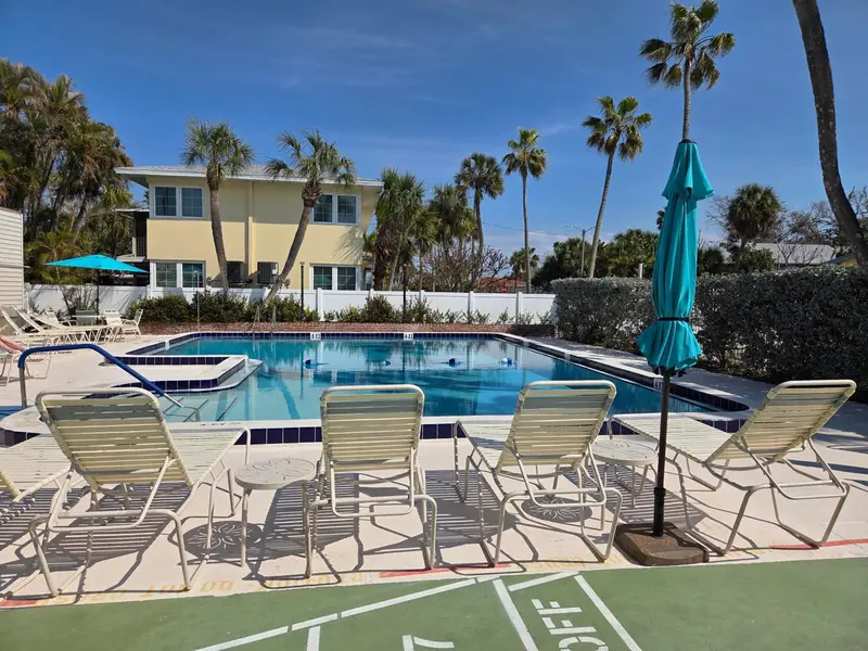 Transats blancs disposés devant une piscine turquoise et un bâtiment jaune clair.