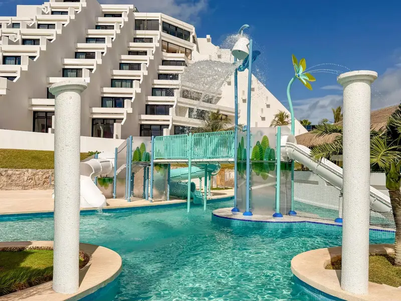 Une piscine avec toboggans et jeux d'eau devant un bâtiment blanc.