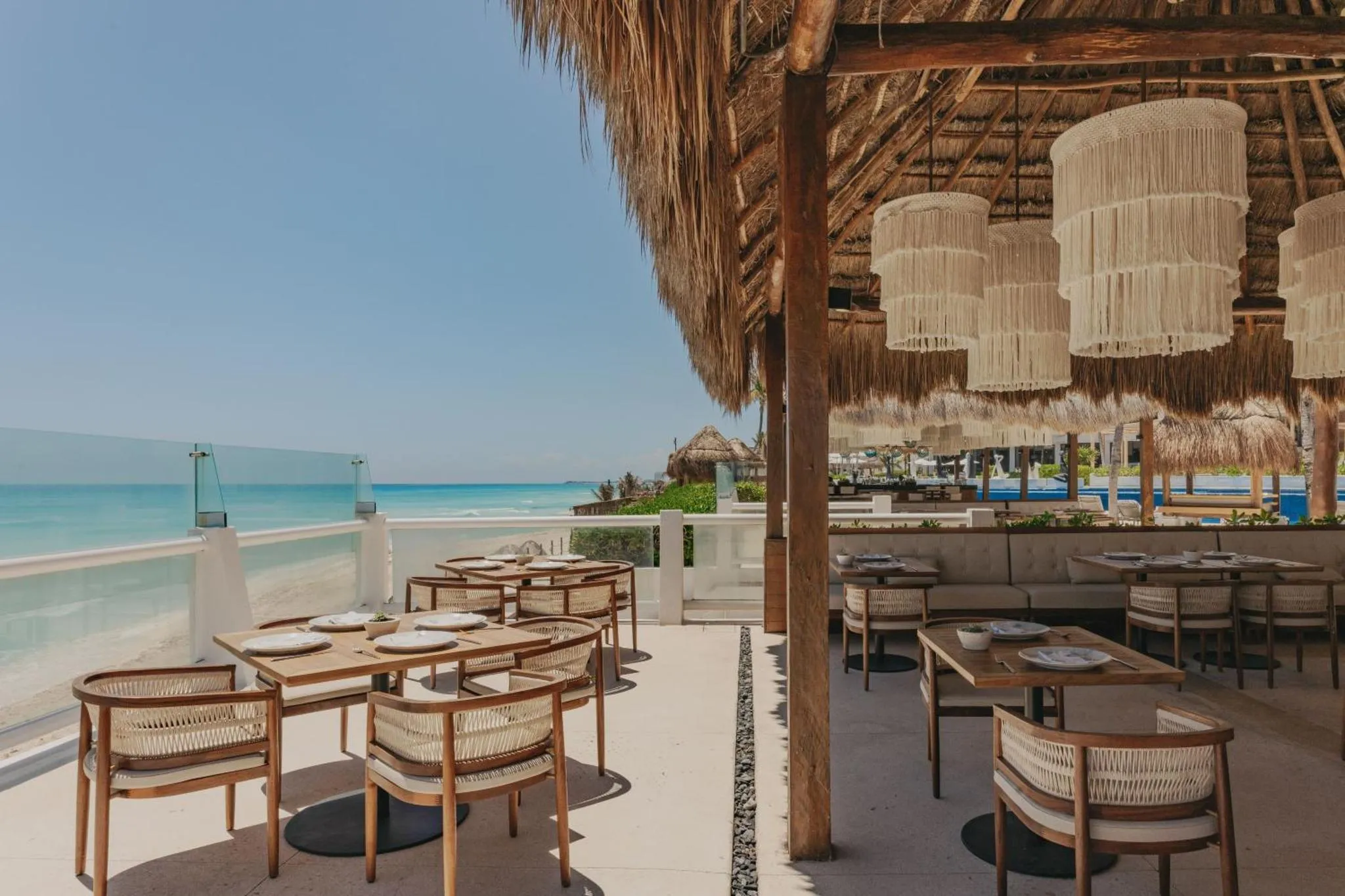 Terrasse ombragée avec tables et chaises face à la mer turquoise.