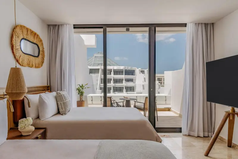 Une chambre lumineuse avec un grand lit et une vue sur la mer depuis une terrasse.
