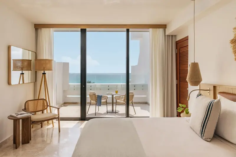 Chambre lumineuse avec un lit et un accès à un balcon donnant sur la mer.