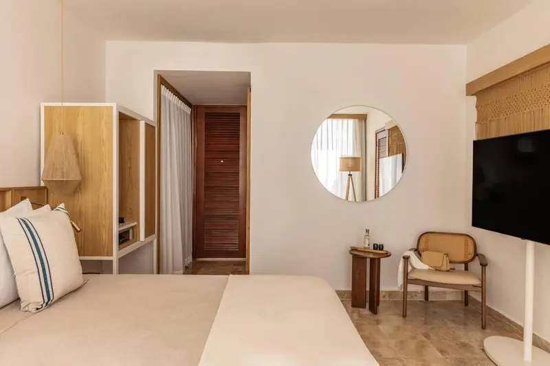 Une chambre lumineuse avec un lit, un fauteuil et un miroir rond.