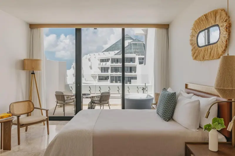 Chambre lumineuse avec un grand lit et une vue sur la mer depuis une terrasse.