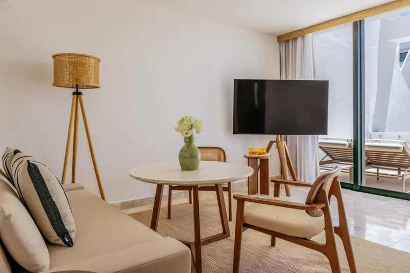 Une pièce lumineuse avec un canapé, une table ronde et une télévision face à une baie vitrée.