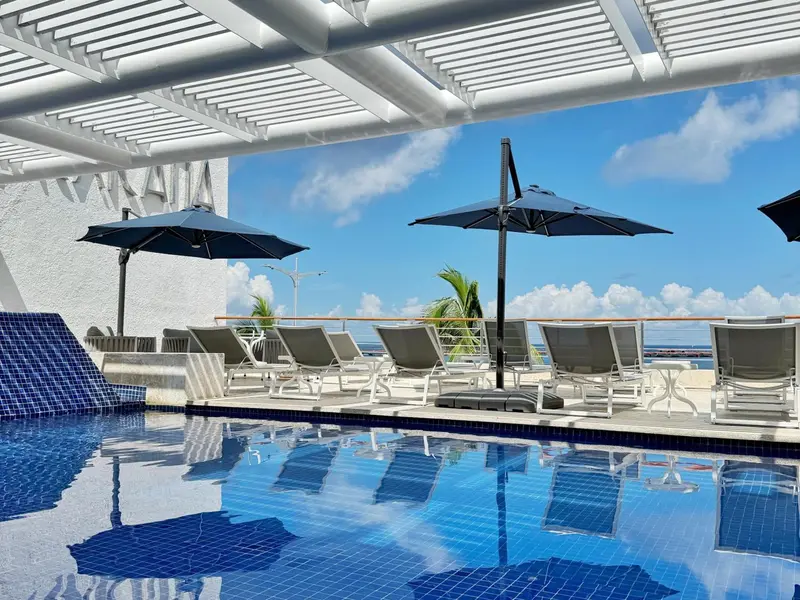 Transats bleus et parasols noirs au bord d'une piscine turquoise.
