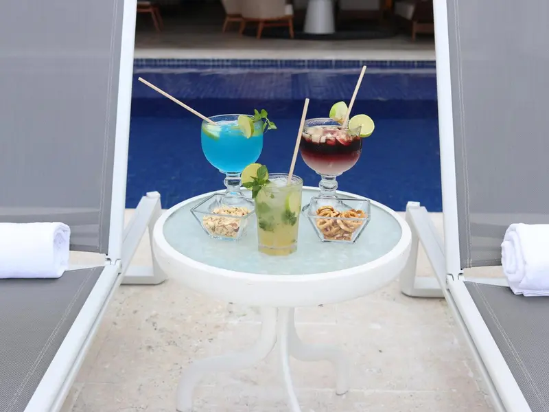 Deux cocktails colorés et des amuse-gueules sont servis sur une table basse au bord d'une piscine.