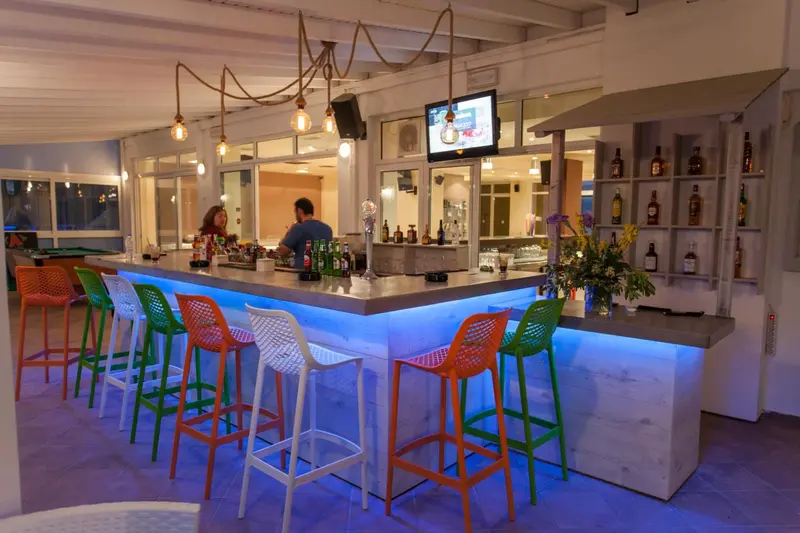 Un comptoir de bar éclairé accueille des clients sur des tabourets colorés.
