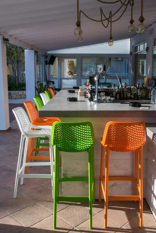 Un comptoir de bar coloré avec des tabourets en plastique est éclairé par des suspensions.
