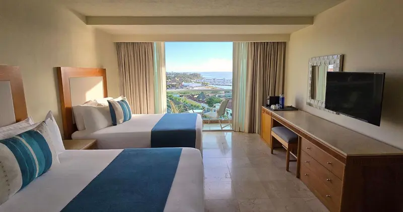 Chambre lumineuse avec deux lits et vue sur la mer.