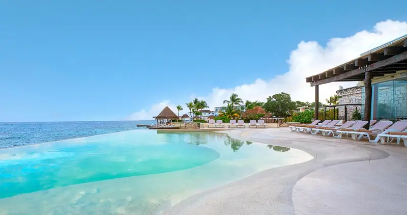 Une piscine à débordement surplombe la mer turquoise et une plage de sable blanc.