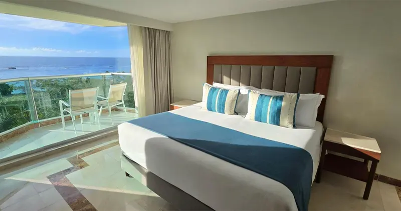 Une chambre lumineuse avec un grand lit et un balcon donnant sur la mer.