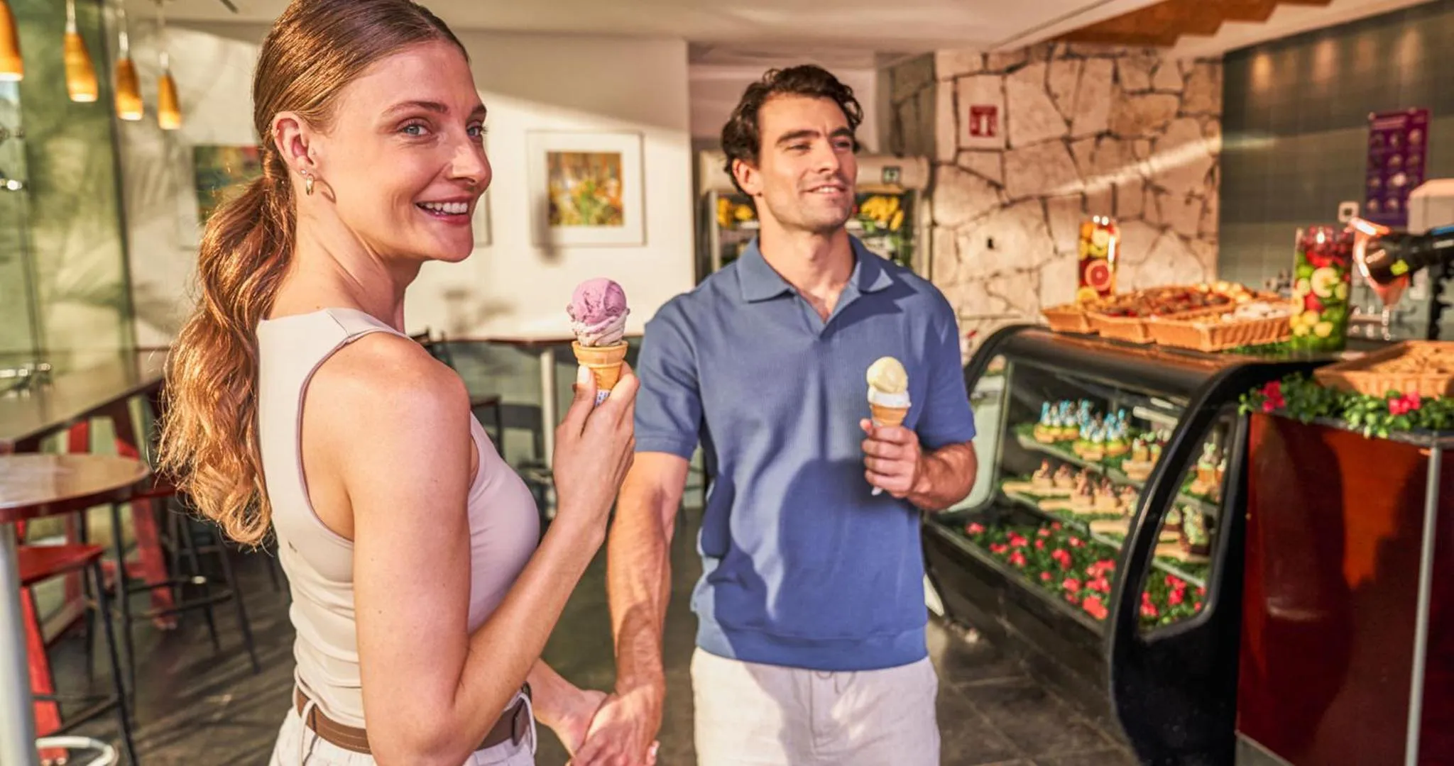 Un couple souriant déguste des glaces devant un comptoir de desserts.