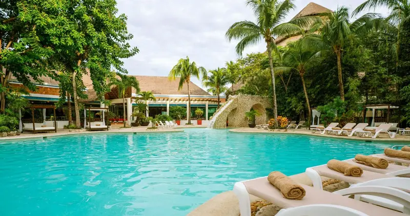 Transats blancs alignés au bord d'une piscine turquoise dans un cadre tropical.