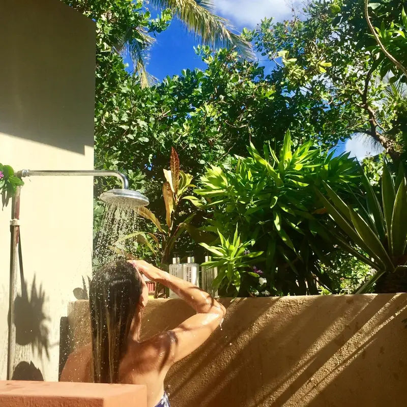 Une personne se douche en plein air, entourée de végétation luxuriante.