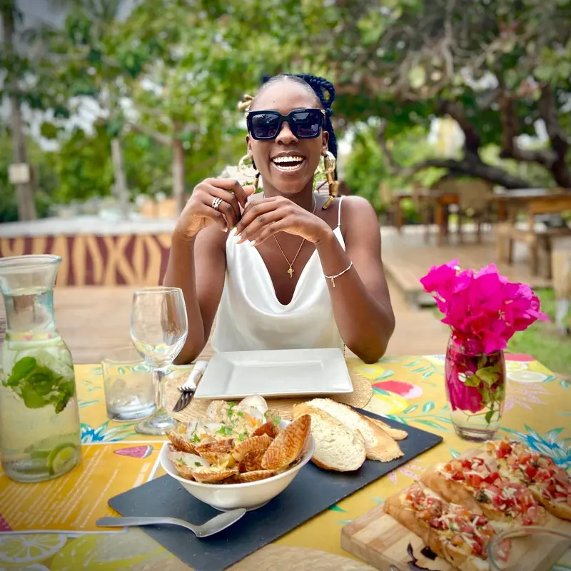 Une personne souriante est assise à une table décorée pour un repas en extérieur.