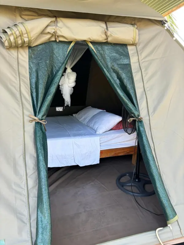Une chambre avec un lit recouvert de moustiquaire est visible à travers l'entrée d'une tente.