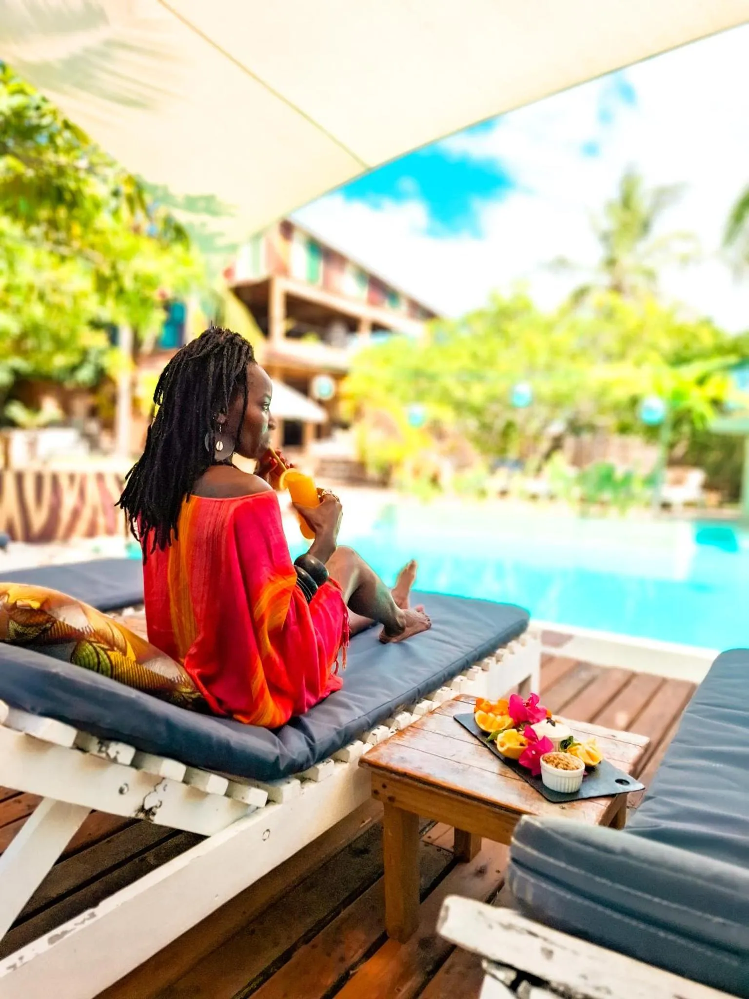 Une personne assise sur un transat déguste un fruit au bord d'une piscine.