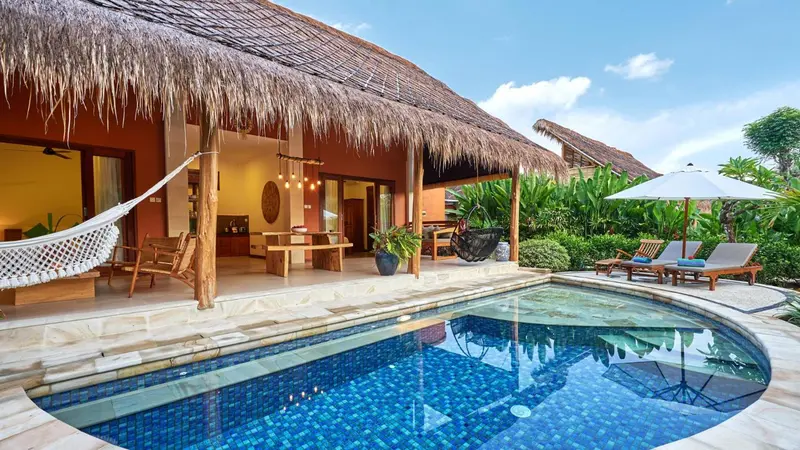 Une terrasse ombragée donne sur une piscine et un jardin tropical.