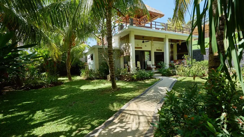 Une allée mène à une villa blanche entourée d'une végétation luxuriante.