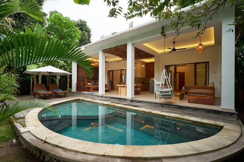 Une piscine bordée d'une terrasse avec mobilier de jardin et un bâtiment blanc en arrière-plan.