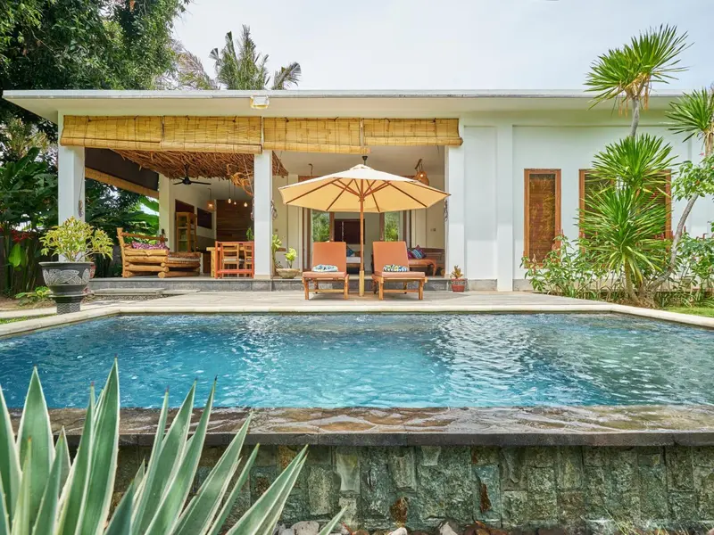 Une piscine turquoise bordée d'une terrasse avec mobilier de jardin devant un bâtiment blanc.