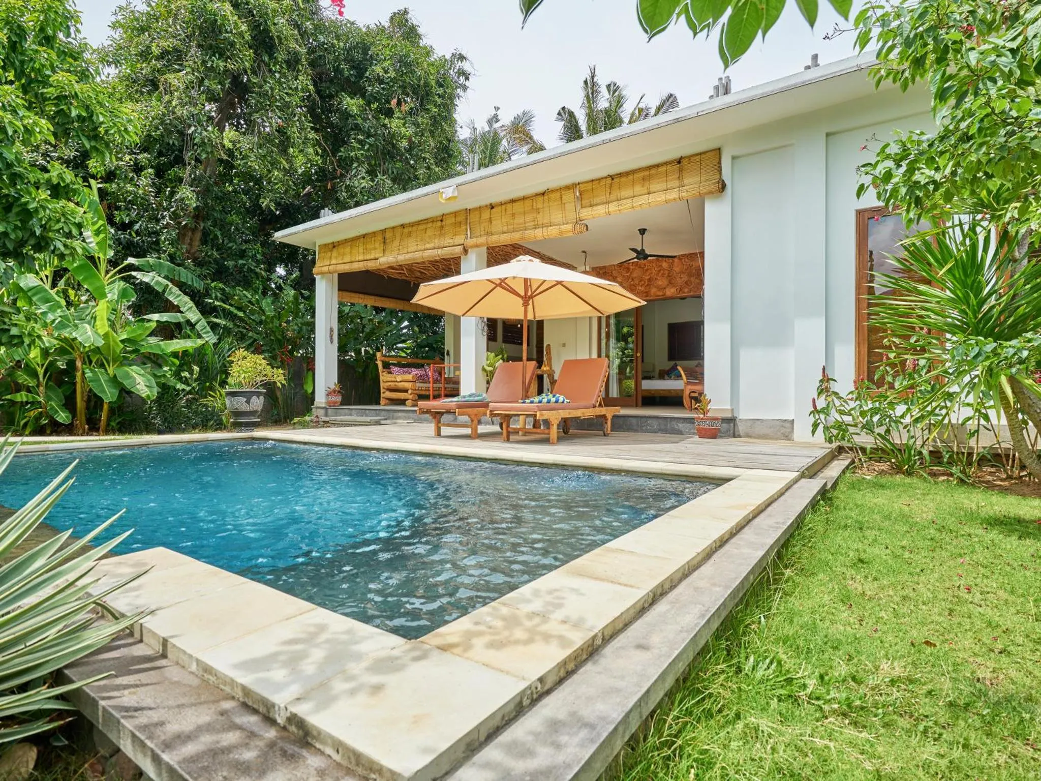 Terrasse ombragée avec transats donnant sur une piscine et un jardin tropical.