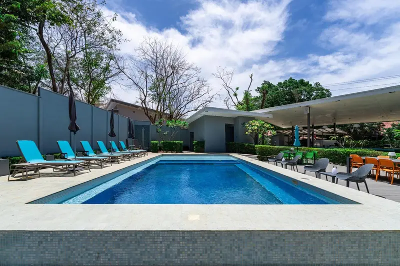 Une piscine rectangulaire bordée de chaises longues et de végétation luxuriante.