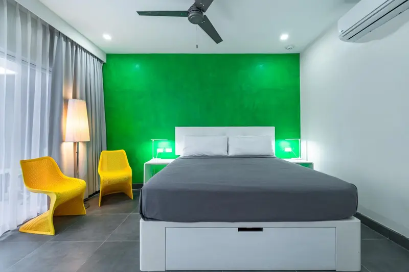 Une chambre lumineuse avec un lit double et deux fauteuils colorés.