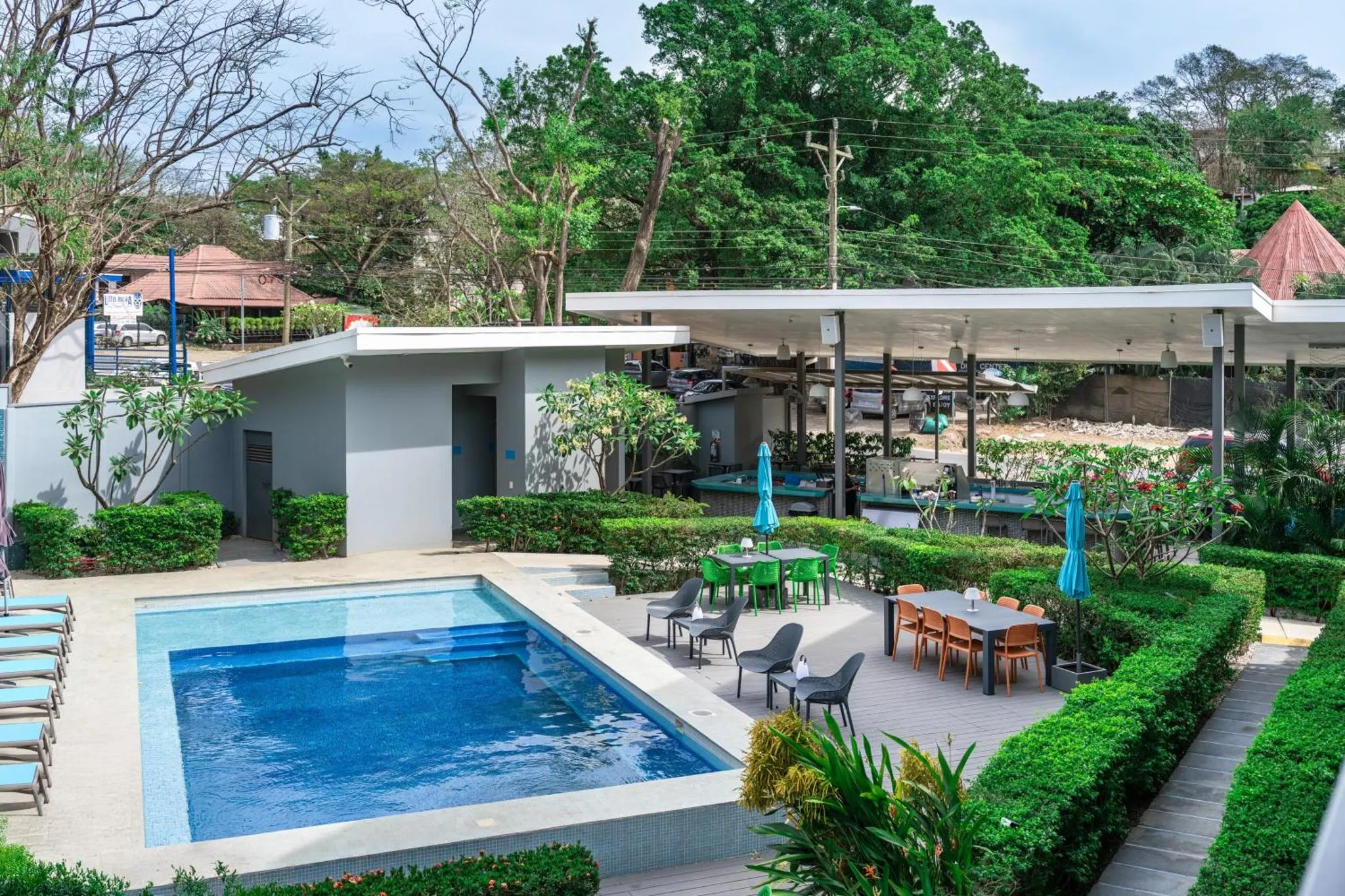 Une piscine rectangulaire turquoise est entourée d'une terrasse aménagée avec des tables et des chaises.