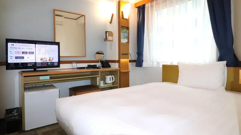 Une chambre d'hôtel lumineuse avec un lit simple et un téléviseur mural.