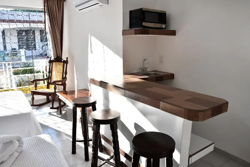 Une kitchenette avec un plan de travail en bois et des tabourets hauts est visible dans une pièce lumineuse.