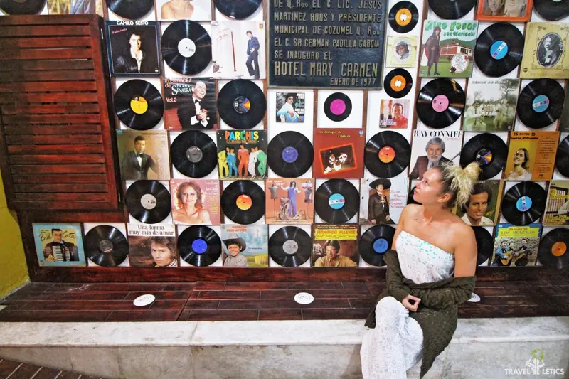 Une femme est assise sur un banc devant un mur décoré de disques vinyles.