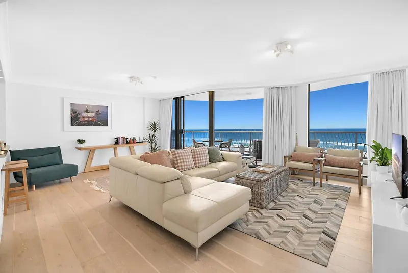 Un salon lumineux avec un canapé d'angle et une vue sur la mer par de grandes baies vitrées.