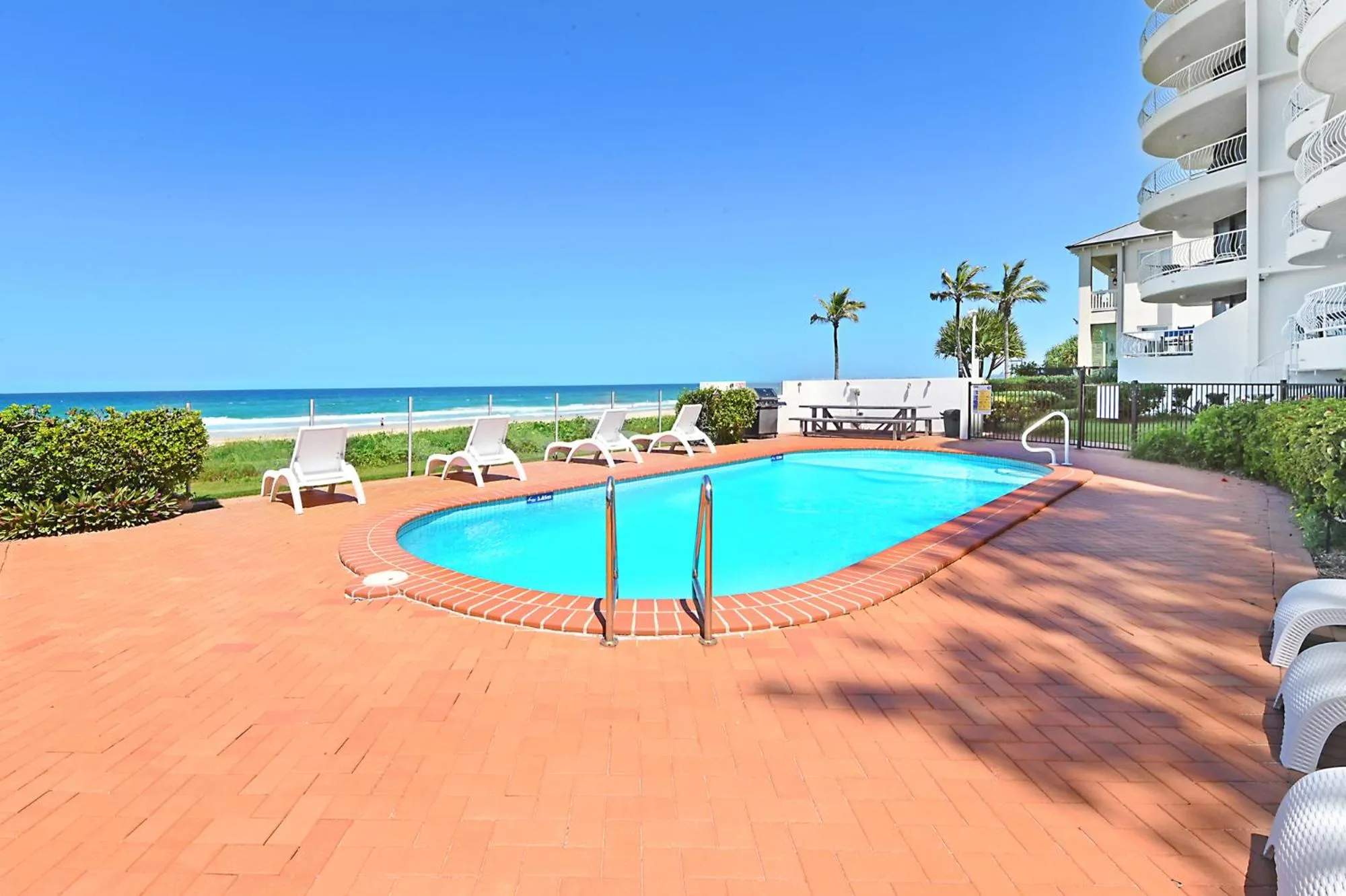 Une piscine rectangulaire bordée d'une terrasse carrelée rouge, avec des transats et la mer en arrière-plan.