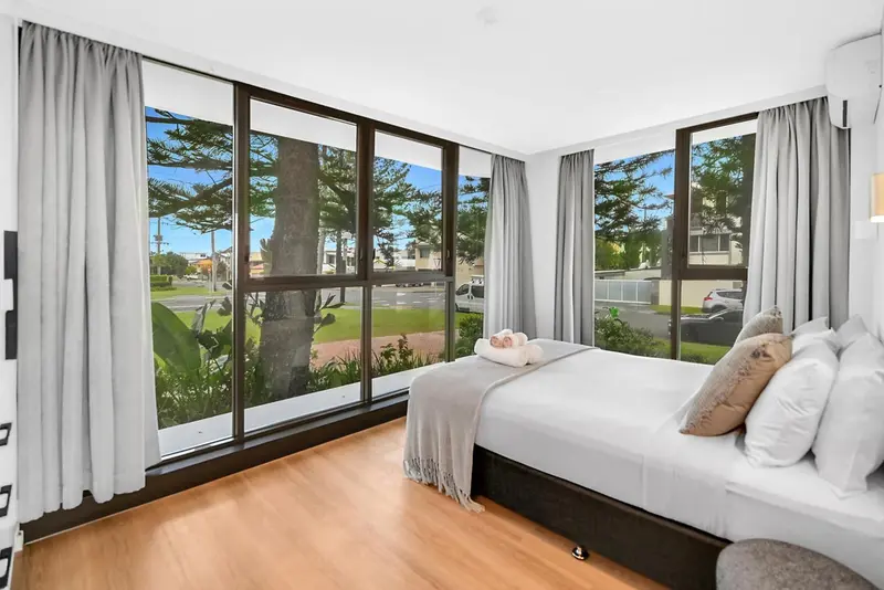 Chambre lumineuse avec un grand lit et vue sur la végétation et la mer.
