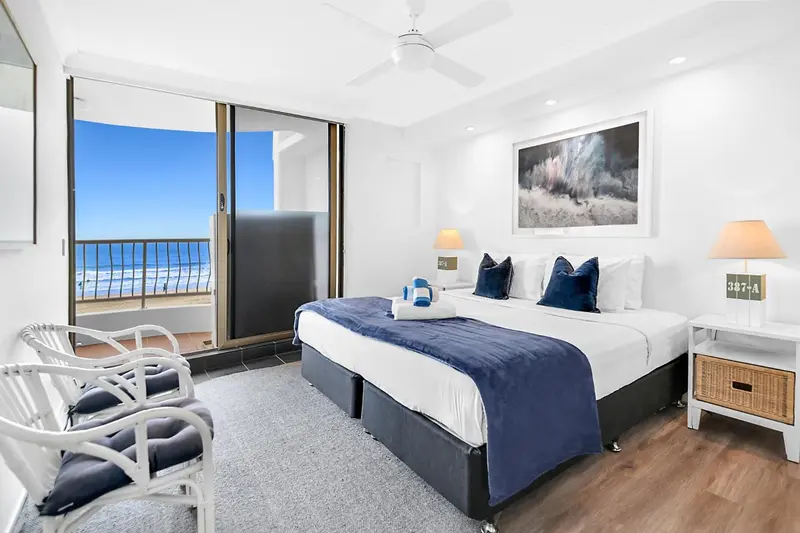 Chambre lumineuse avec un grand lit et vue sur la mer depuis un balcon.