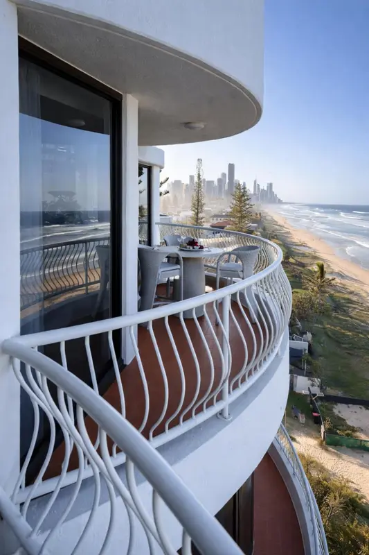 Vue d'un balcon avec une table et des chaises donnant sur la mer et la ville.