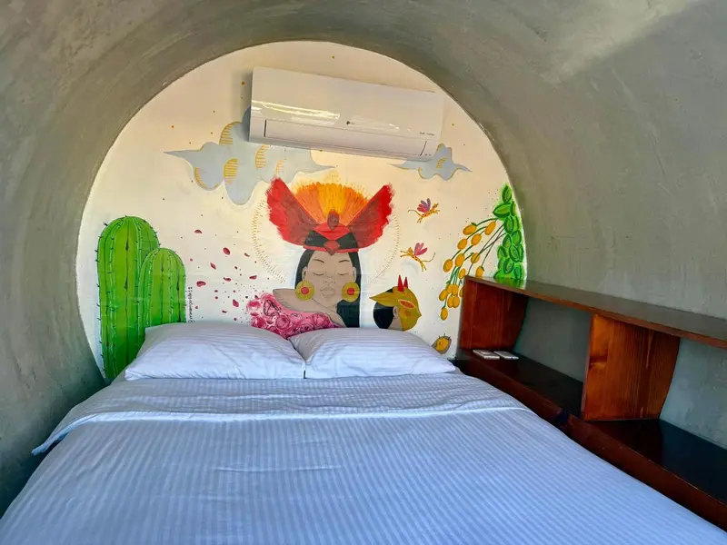 Un lit blanc est dispose dans une chambre aux murs courbes decores d'une fresque colorée.