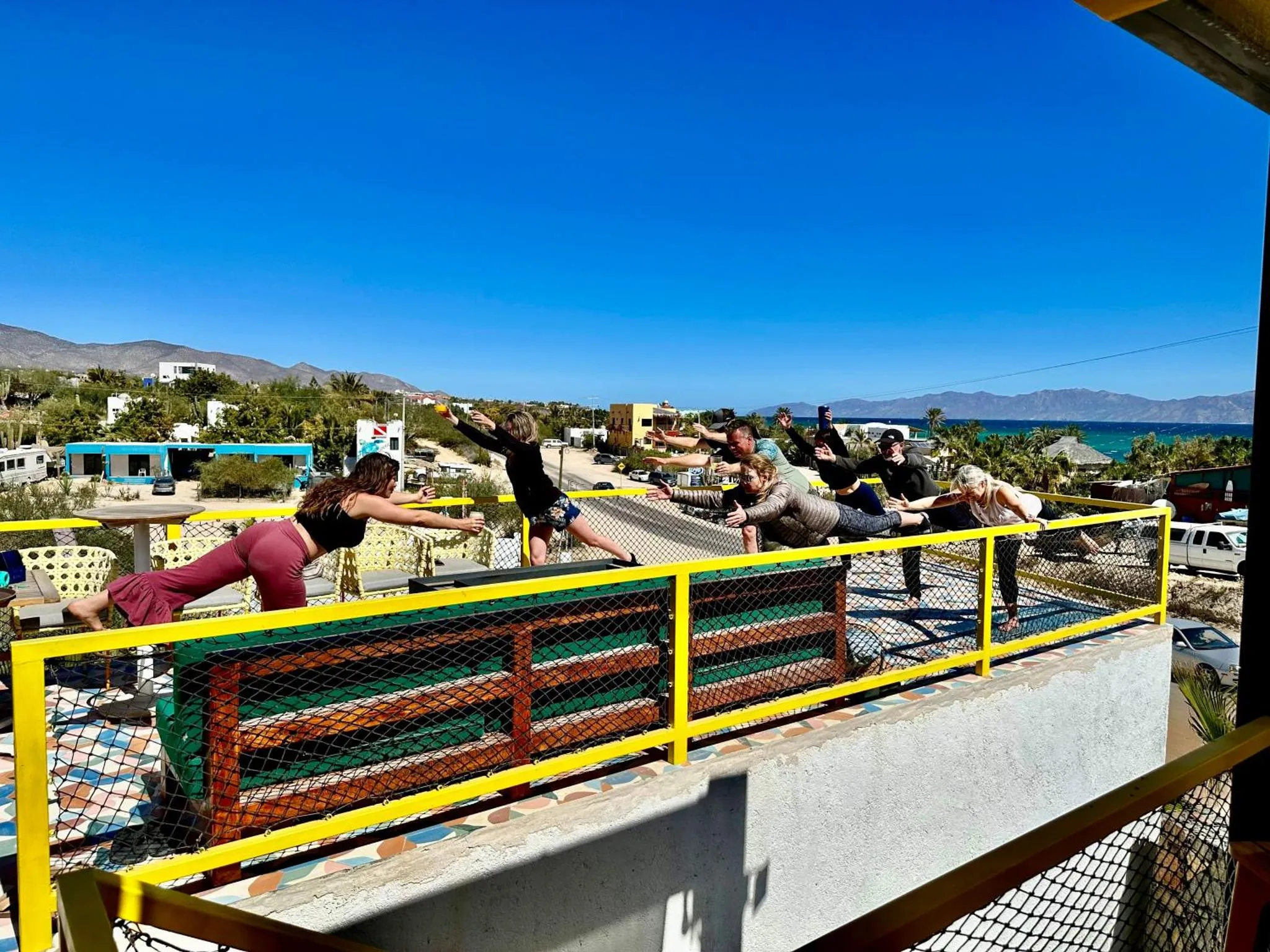 Un groupe de personnes s'étire sur une terrasse ensoleillée avec vue sur la mer et les montagnes.