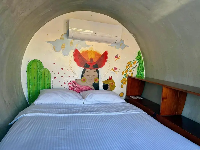 Lit blanc immaculé dans une chambre aux murs courbés décorée d'une fresque colorée.