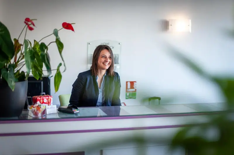 Une employée souriante se tient derrière un comptoir d'accueil.