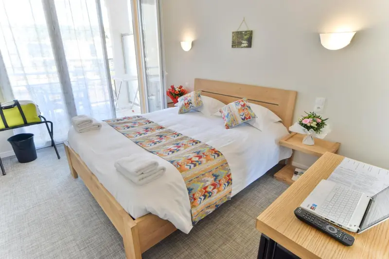 Une chambre lumineuse avec un grand lit recouvert d'une courtepointe colorée et des fleurs fraîches.