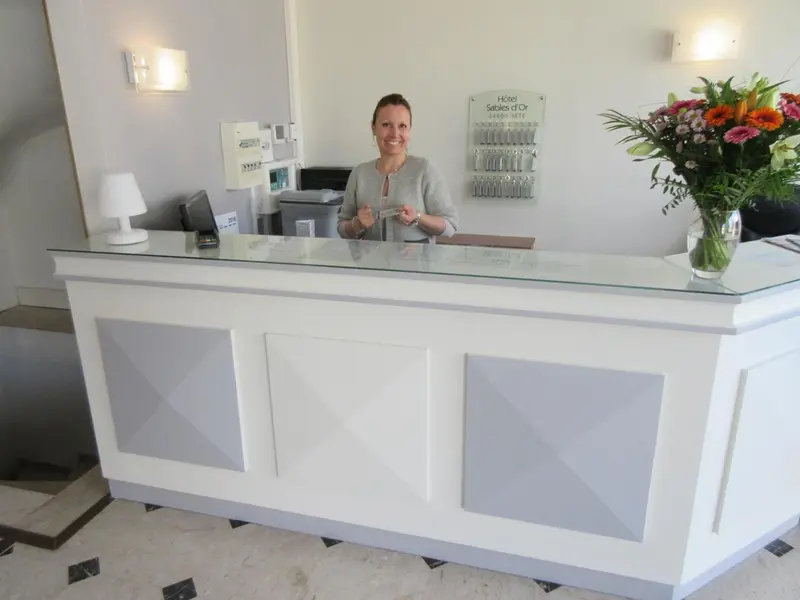 Une employée souriante se tient derrière le comptoir d'accueil d'un hôtel.
